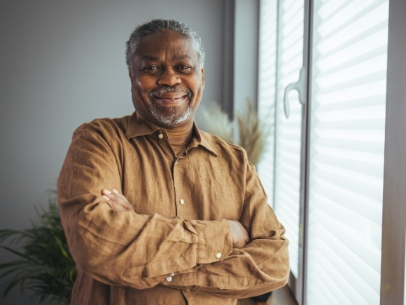 Photo of a elderly man looking towards the camera smiling with his arms crossed.