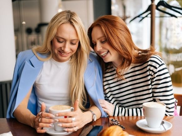 Photo of two friends laughing together having coffee.