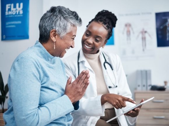 A doctor points at a tablet and smiles at her patient who looks overjoyed.
