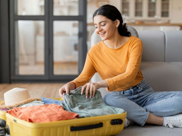 Photo of a lady sat on her floor packing her suitcase.