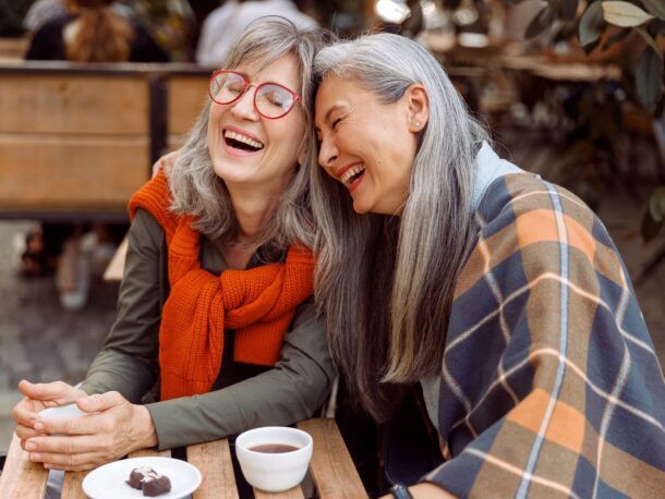 Photo of two women sitting in a cafe laughing together.