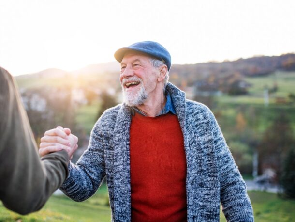 Photo of an elderly man shaking hands with another man outside in a field.