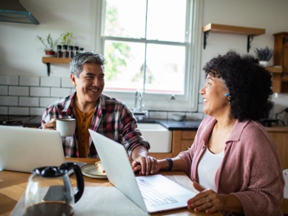 Image of a man and woman sat at a breakfast table using their laptops