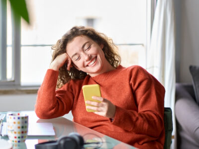 Image of a lady sat at a desk looking down at her mobile phone smiling