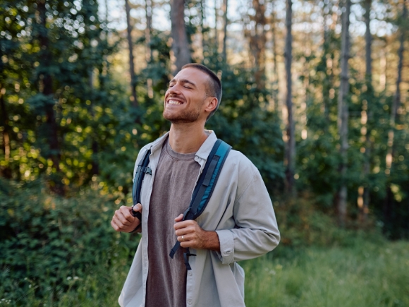 Photo of a young man wearing a backpack walking through woodland.