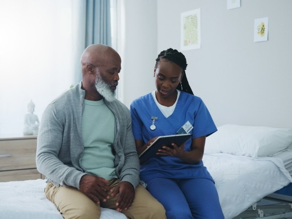 Image of a female nurse speaking with a male patient, they are looking at notes on a tablet together