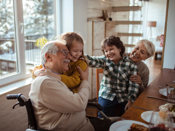 Image of grandparents sitting at a table hugging their grandchildren