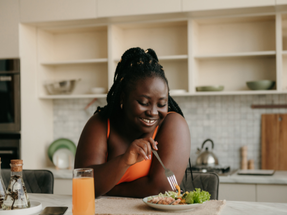 Photo of a lady leaning on a kitchen counter eating chicken and salad