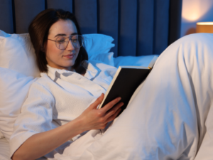 Photo of a young woman sat in bed reading a book