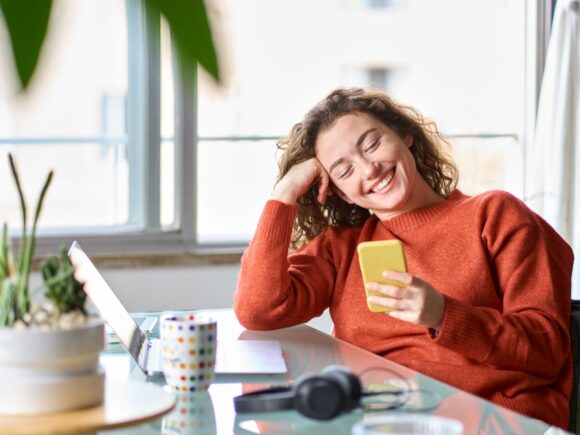 Image of a lady sat at a desk looking down at her mobile phone smiling